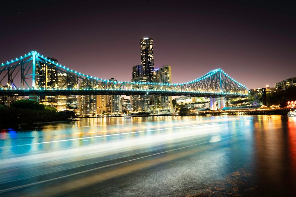 Bright cityscape view of Story Bridge in Brisbane at night with vibrant reflections on the river.